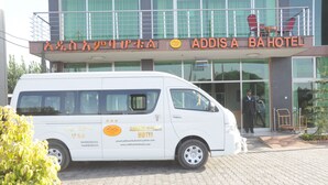 A white van parked in front of Addis Ababa Hotel with contact information and a website URL visible on its side. - Addis Amba Hotel (Bahir Dar)
