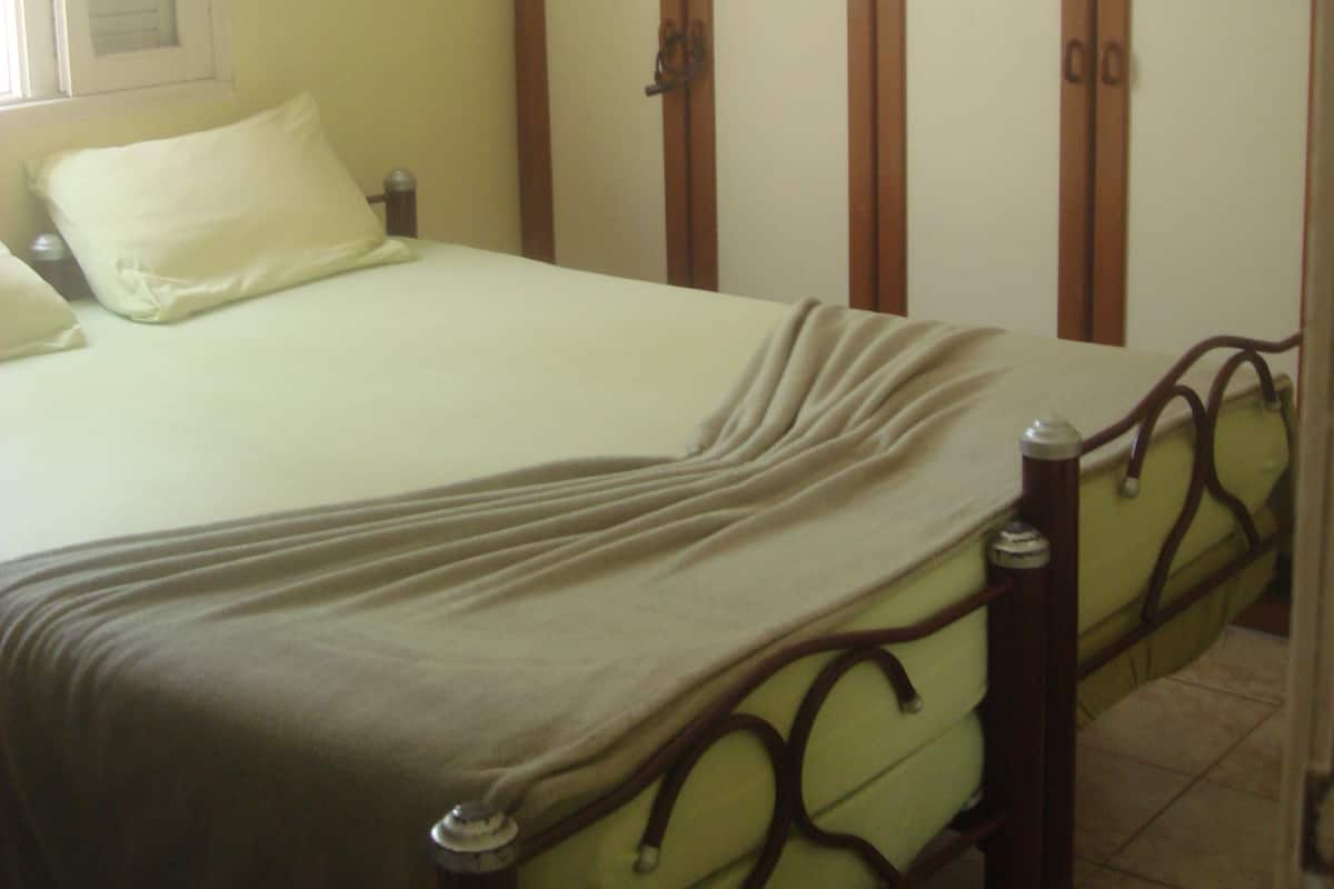 A bed with a metal frame and a headboard, a bedside table, and a window with blinds.
