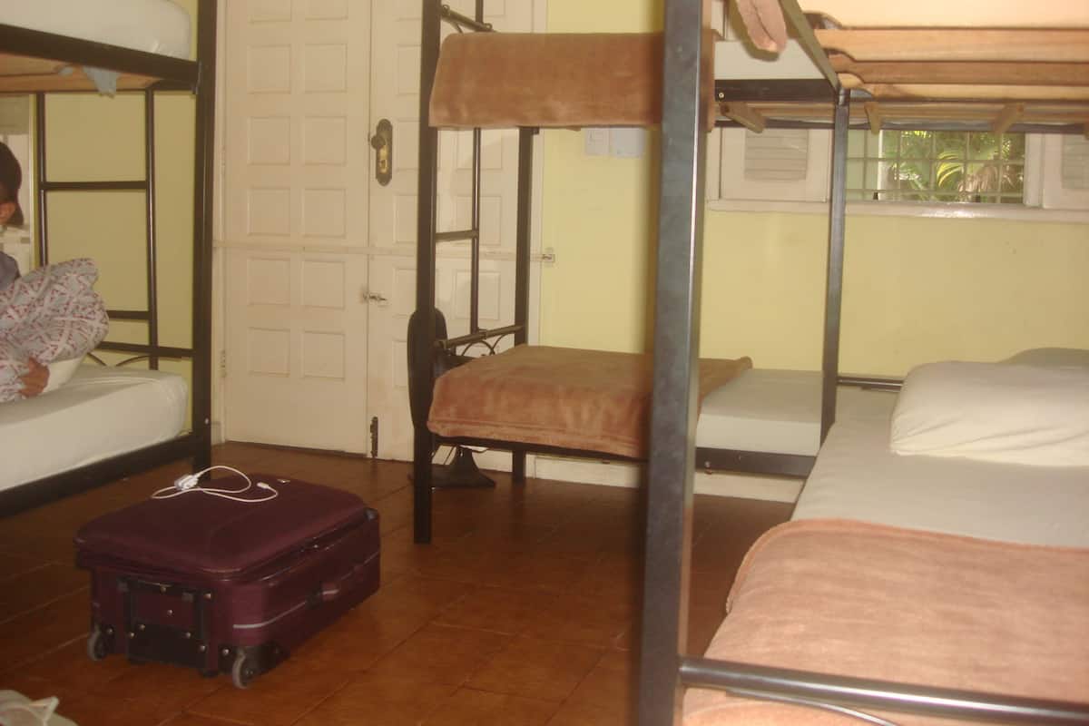 A dormitory room with bunk beds, a suitcase, and a fan.