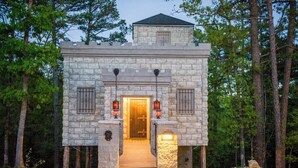 A stone building with a wooden door, steps leading up to it, and lanterns on either side. - Eureka Springs Treehouses, Hobbit Caves & Castles (Eureka Springs)