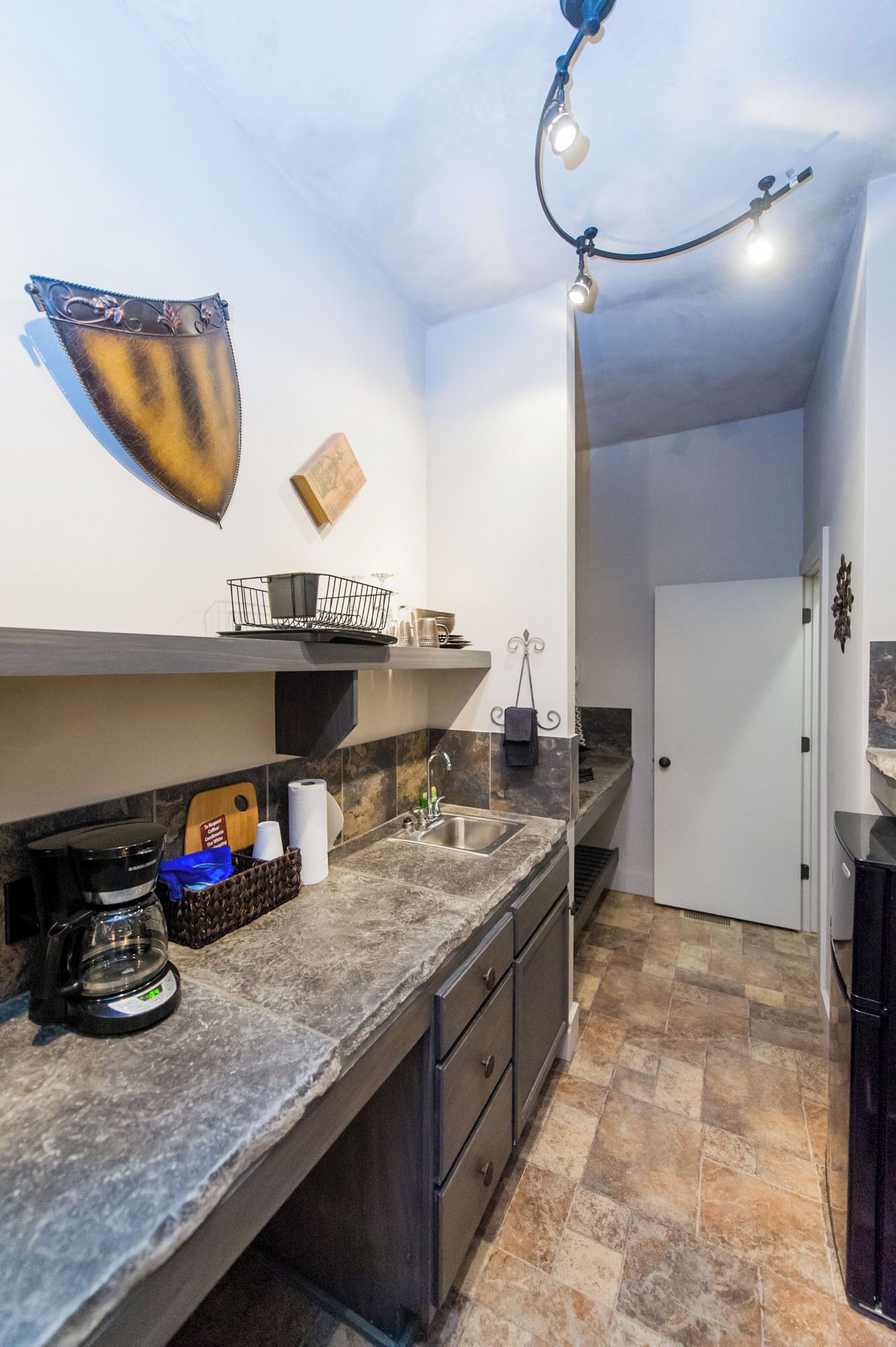 A compact kitchen with a marble countertop, a coffee machine, and a hanging light fixture.