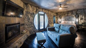 A bedroom with a stone wall, a fireplace, a large bed, and a ceiling fan. - Eureka Springs Treehouses, Hobbit Caves & Castles (Eureka Springs)