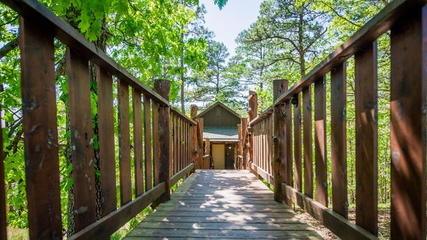A wooden pathway leading to a building surrounded by trees. - Eureka Springs Treehouses, Hobbit Caves & Castles (Eureka Springs)