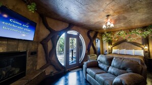 A cozy room with a fireplace, a leather sofa, and a large window. - Eureka Springs Treehouses, Hobbit Caves & Castles (Eureka Springs)