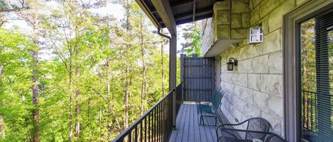 A wooden deck with metal chairs and a table, overlooking a forested area.