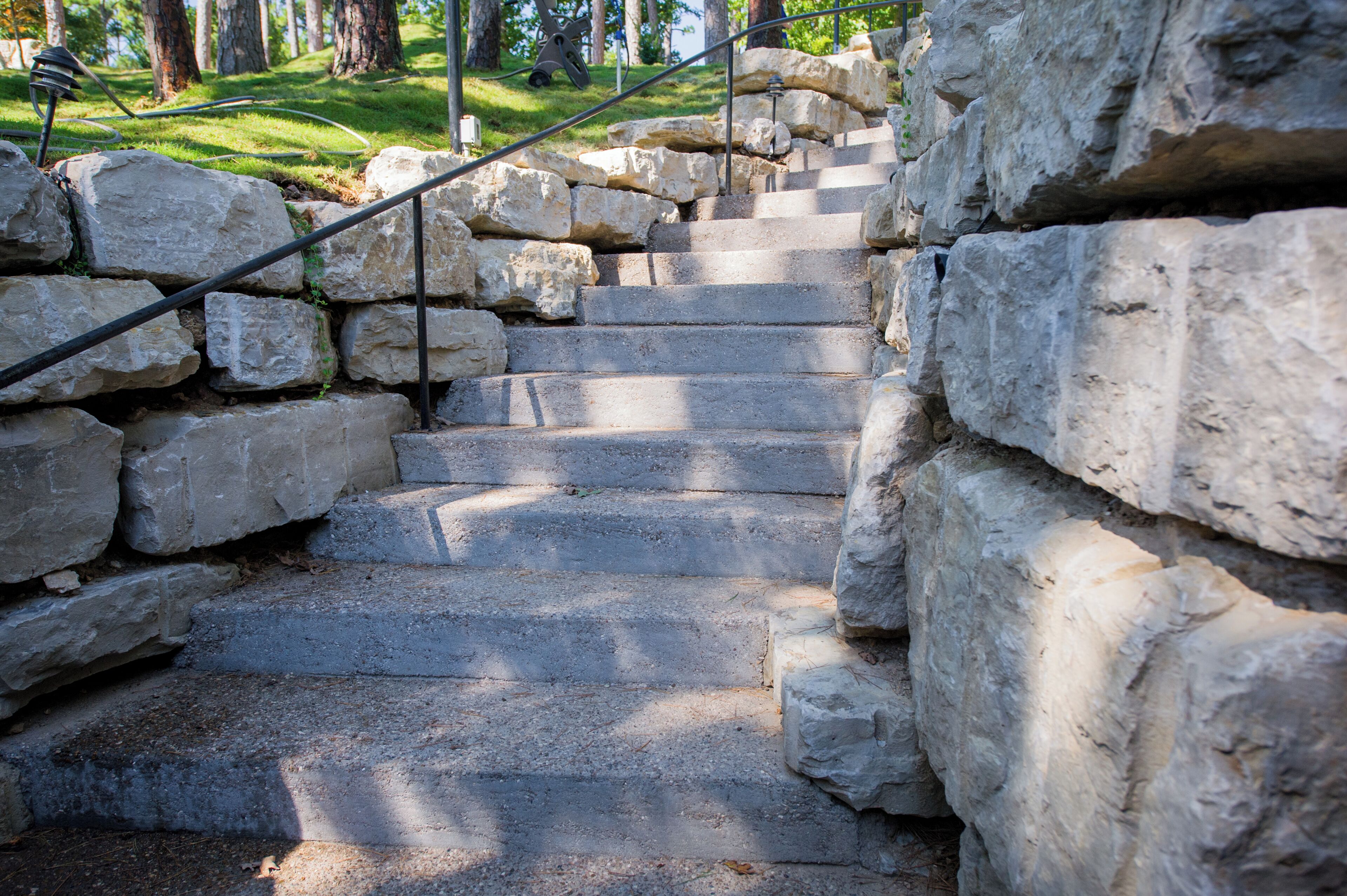 A stone staircase with metal railings, surrounded by large rocks and trees.