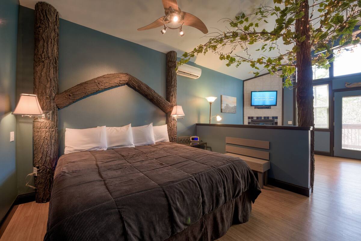 Un dormitorio con una cama grande, vigas de madera, un ventilador de techo y un televisor en la pared.