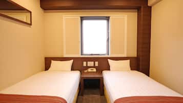 A hotel room with two single beds, a small bedside table with a phone, and a window above the beds.
