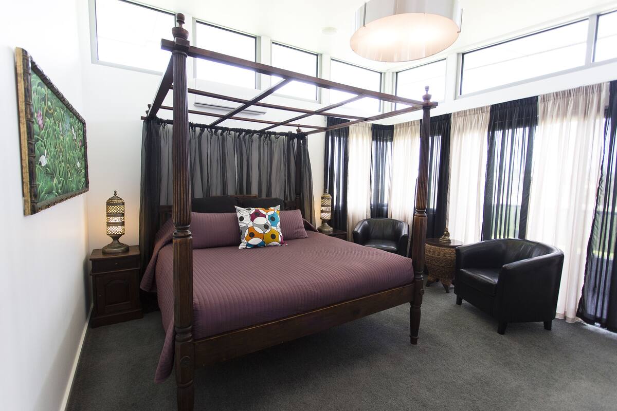 A four-poster bed with a purple bedspread, a decorative pillow, and a nightstand with a lamp.