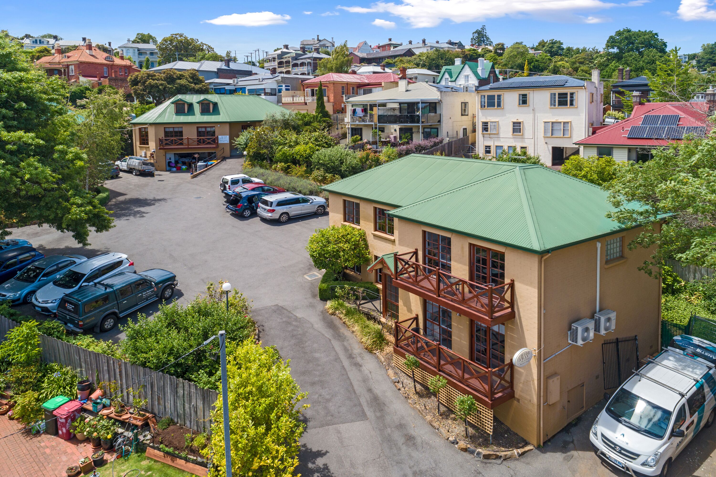 A residential area with a two-story house featuring a green roof, a balcony, and a small garden.