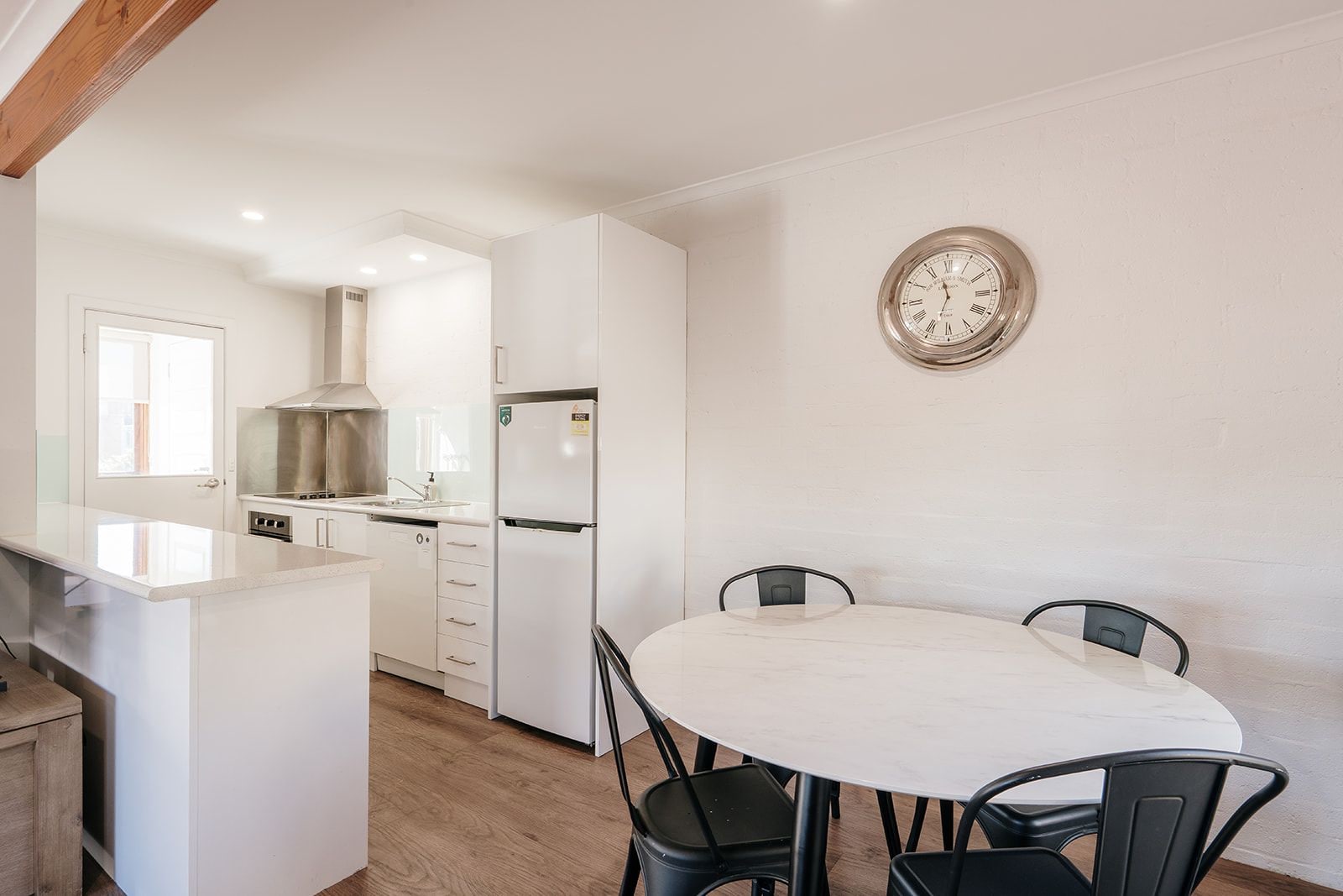 Una cocina moderna con muebles blancos, horno empotrado y zona de comedor con una mesa y sillas redondas.