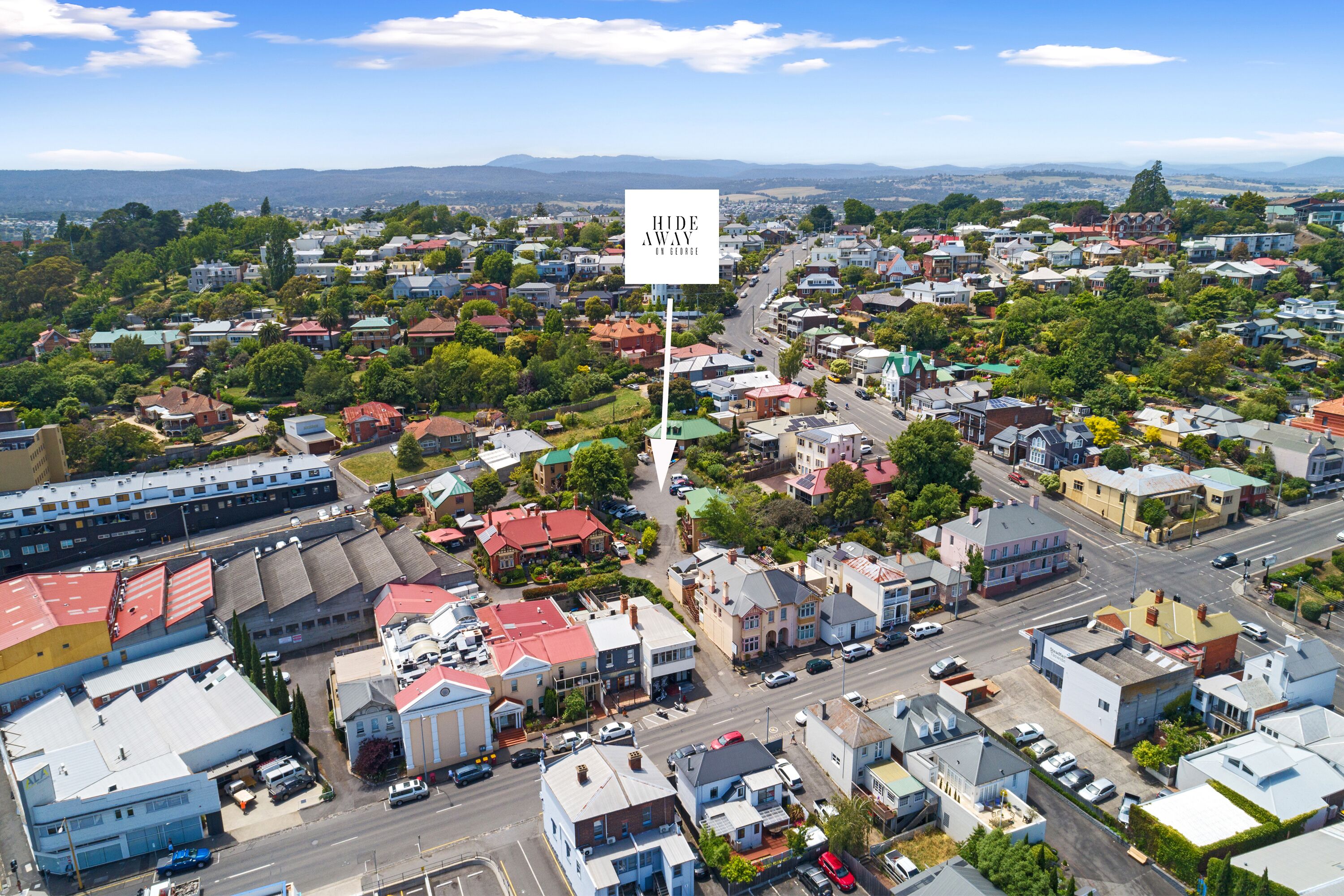 Vista aérea de un pueblo con edificios residenciales y comerciales, una importante intersección de calles y un anuncio publicitario.