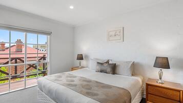 A bedroom with a large window, a bed with a patterned bedspread, two bedside tables with lamps, and a framed picture on the wall.