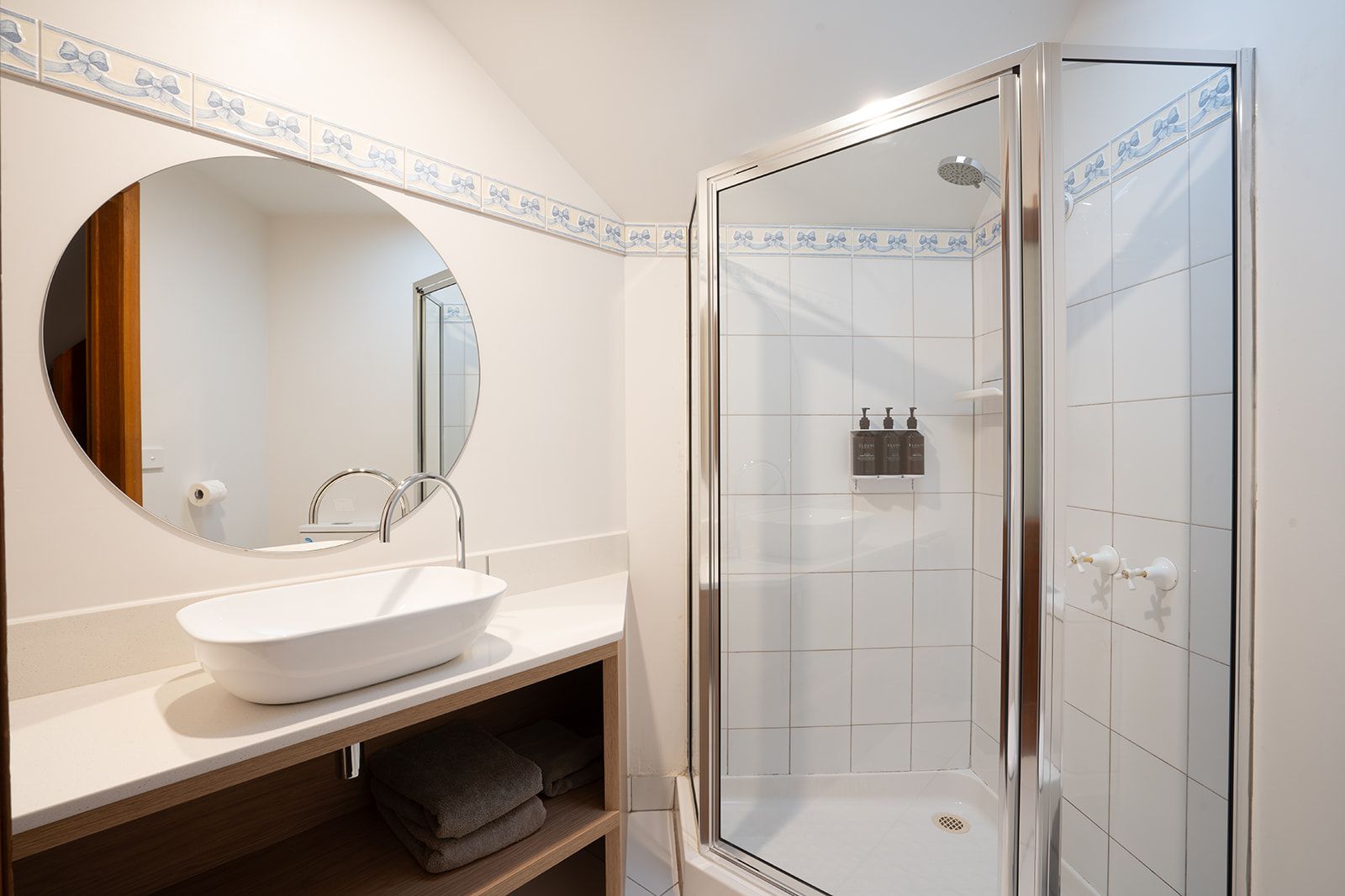 A bathroom with a round mirror, a white sink, a glass shower enclosure, and a towel rack.