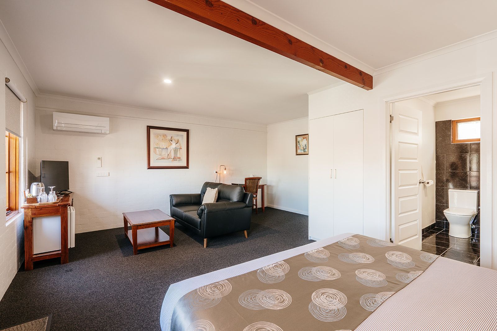 Habitación de hotel con cama, sofá, una mesita, televisor y baño con inodoro y lavamanos.