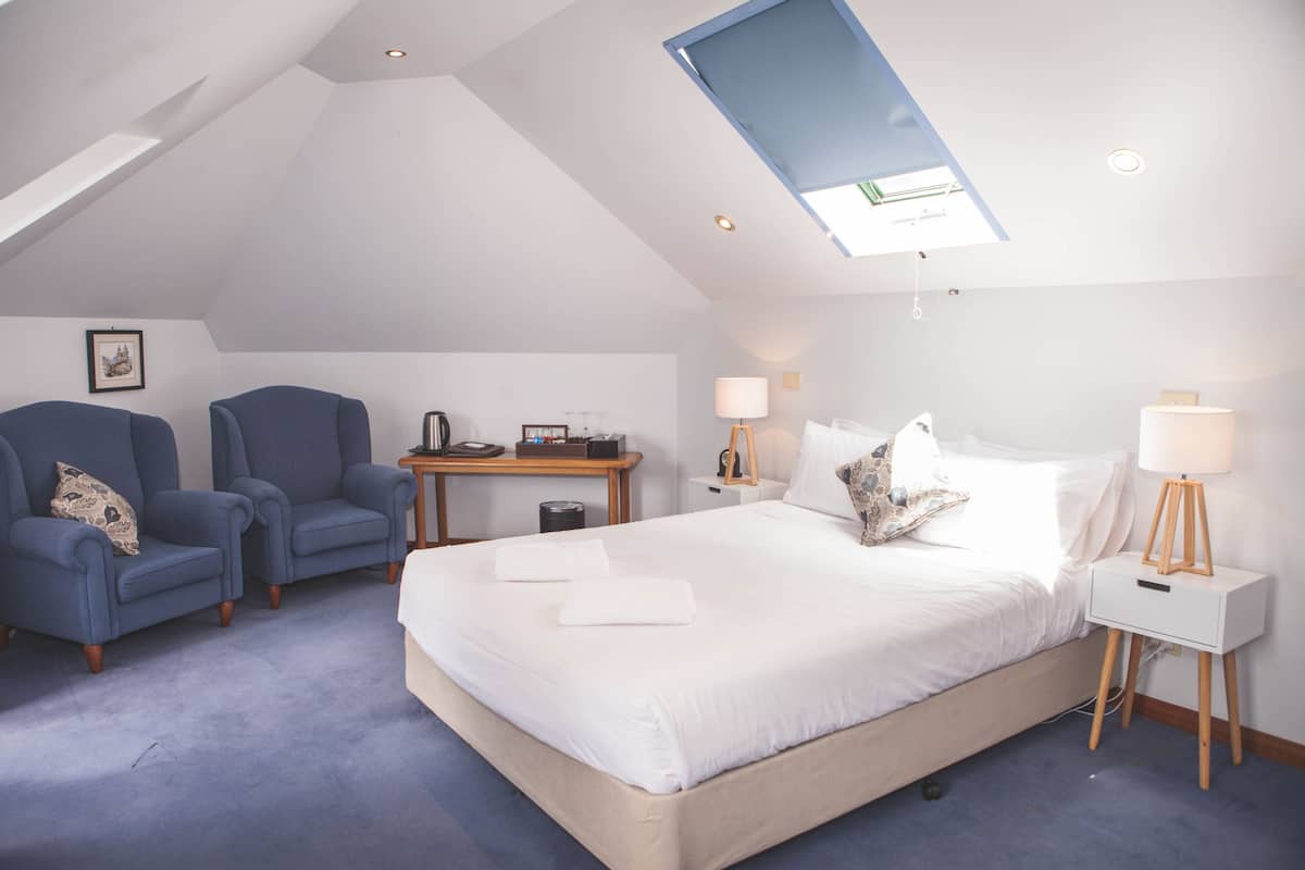 A bedroom with a large bed, two armchairs, a desk with a lamp, and a skylight.