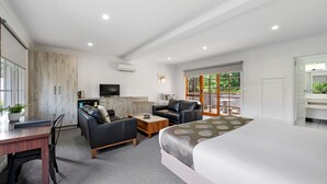 A modern hotel room with a large bed, a sofa, a coffee table, a TV, and a window with a view of greenery.