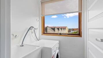 A compact laundry room with a washing machine, a sink, and a window with a view of buildings.