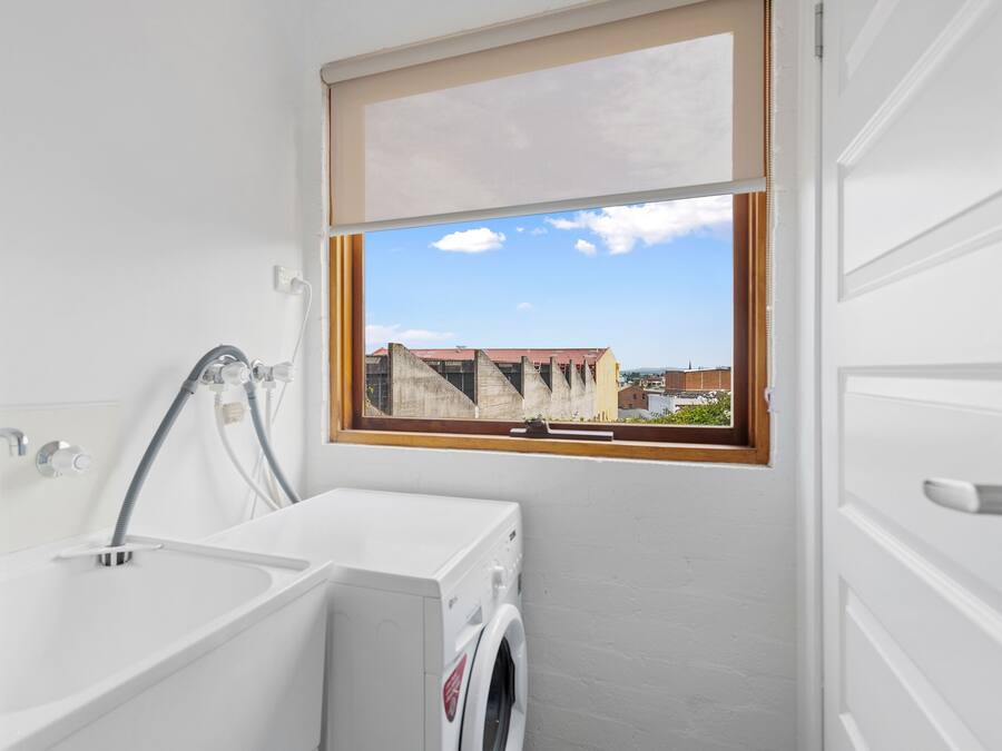 A compact laundry room with a washing machine, a sink, and a window with a view of buildings.