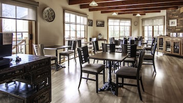 A spacious dining area with multiple tables and chairs, wooden floors, and large windows allowing natural light.