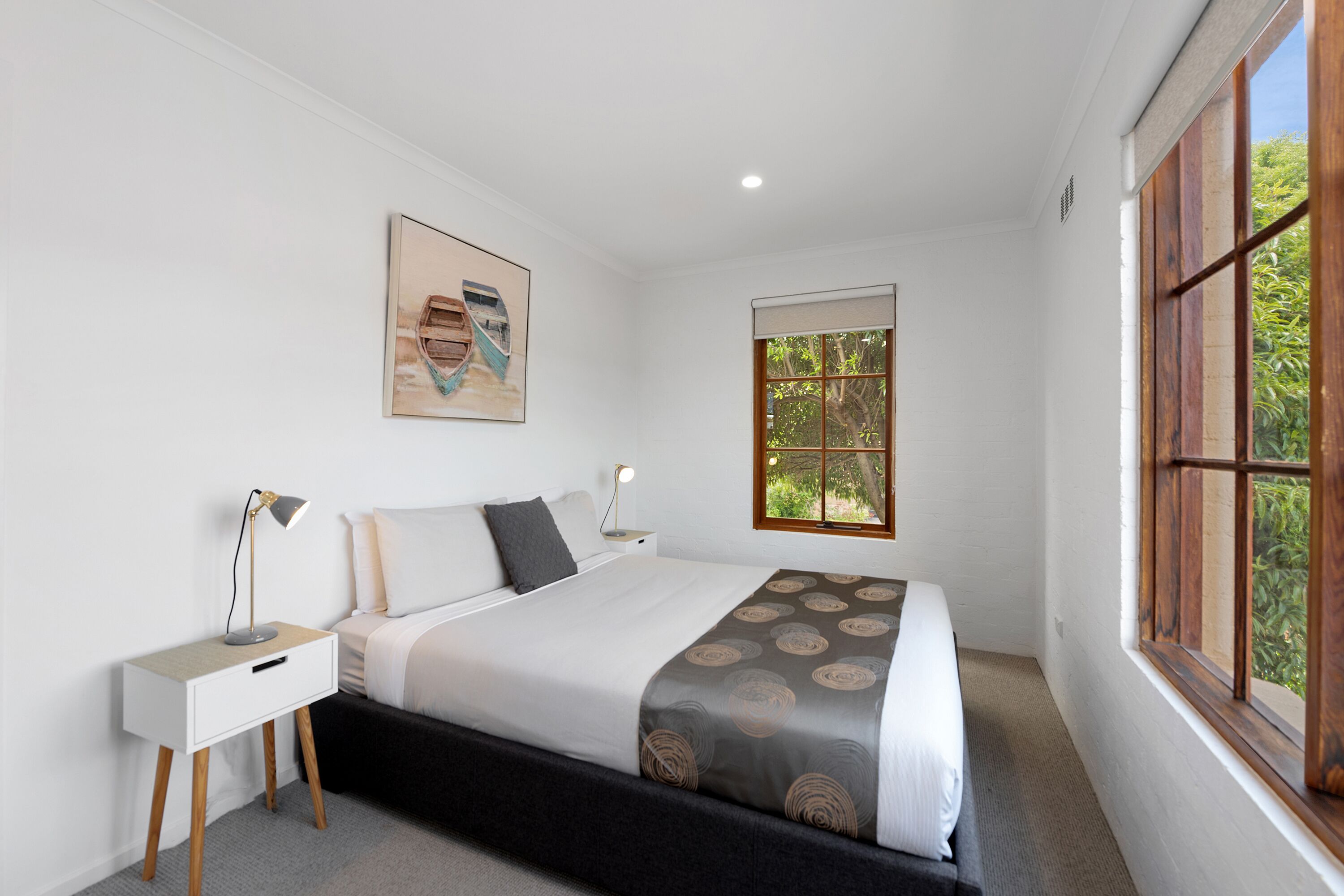 A bedroom with a bed, bedside tables, a window, and a painting on the wall.