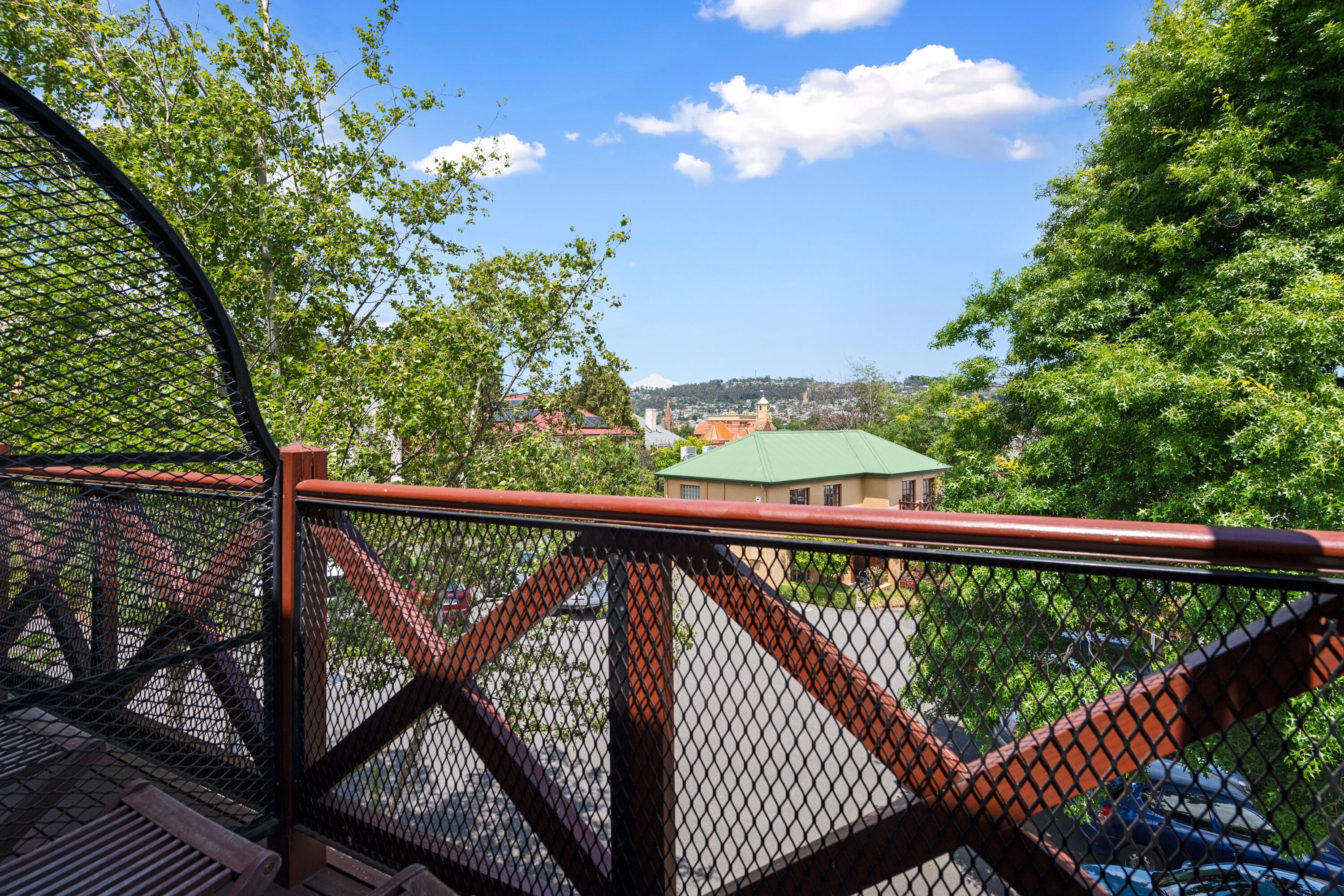 A view from a balcony with a metal railing, overlooking a parking area and buildings with green roofs.