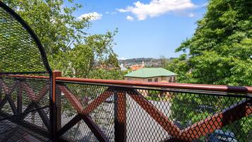 A view from a balcony with a metal railing, overlooking a parking area and buildings with green roofs.
