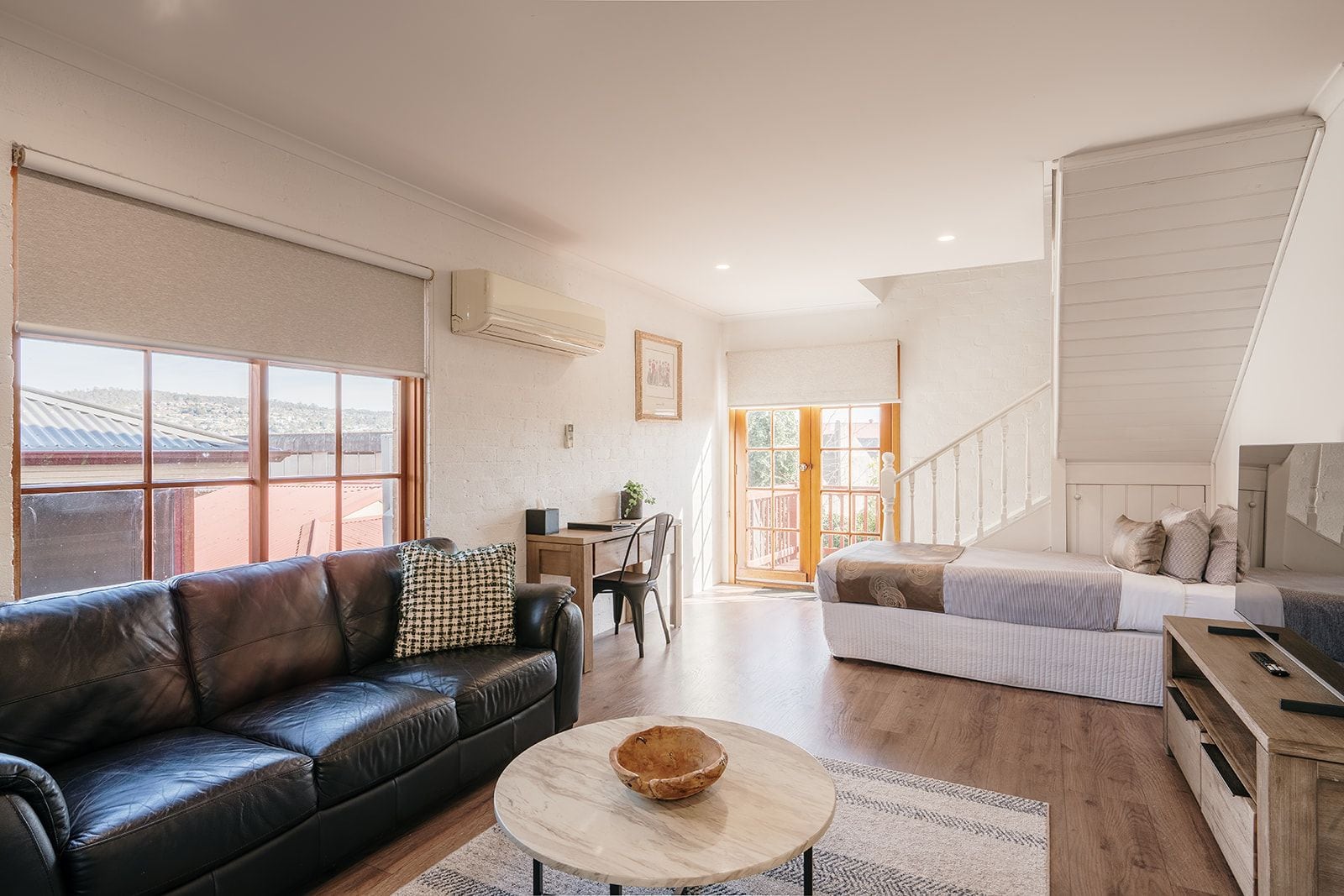 A spacious living area with a leather sofa, a round coffee table, and a staircase leading to an upper level.