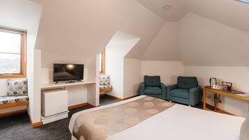 Habitación de hotel moderna con cama, escritorio con televisor, dos sillones y una mesita con hervidor.