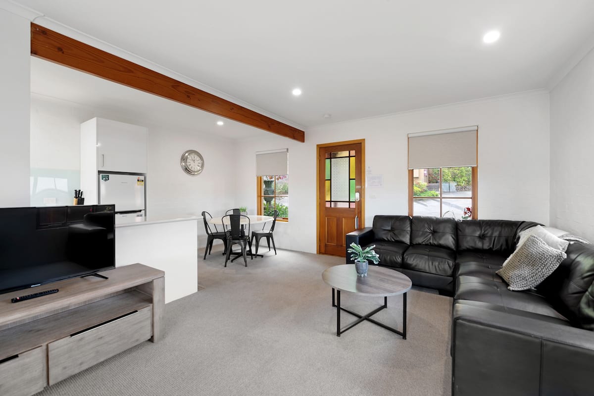 A modern living room with a flat-screen TV, a leather sofa, a dining table with chairs, and a small coffee table.