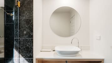 Un baño moderno con tocador blanco, espejo redondo y cabina de ducha de mármol negro.