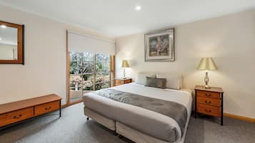 A bedroom with a large bed, two bedside tables with lamps, a bench, a window with a view, and a framed picture on the wall.