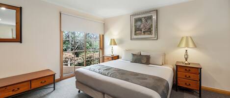 Un dormitorio con una cama grande, dos mesitas de noche con lámparas, un banco, una ventana con vistas y un cuadro enmarcado en la pared.