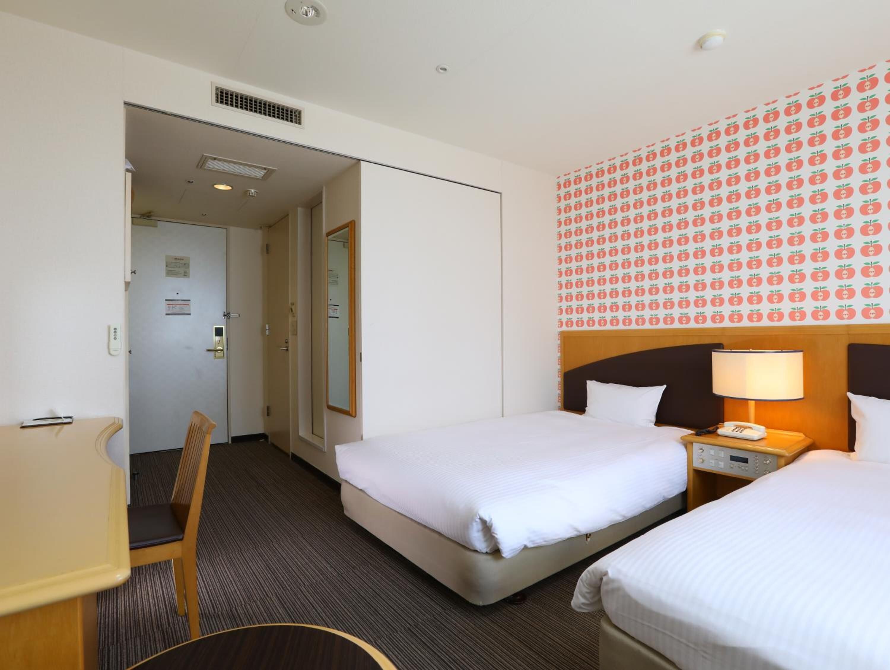 Ein Hotelzimmer mit zwei Betten, einem Schreibtisch, einem Stuhl und einem durch eine geöffnete Tür einsehbaren Badezimmer.