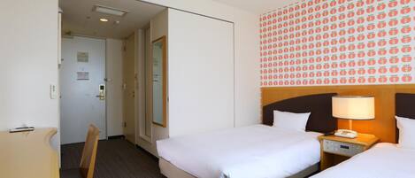 A hotel room with two beds, a desk, a chair, and a bathroom visible through an open door.