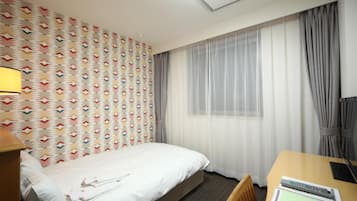 A hotel room with a bed, a desk, and a window with sheer curtains.