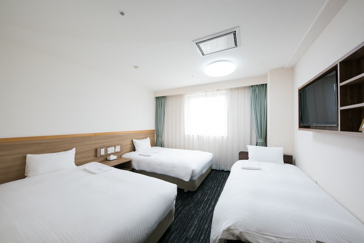 Ein Hotelzimmer mit zwei Betten, einem Schreibtisch, einem Stuhl, einem Fernseher und einem Fenster mit Vorhängen.