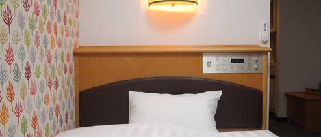 A hotel room with a bed, a wall-mounted control panel, and a patterned wallpaper on the left.