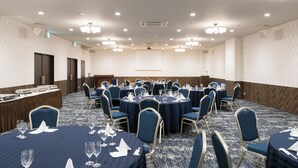 Un salón de conferencias con mesas redondas, sillas azules y manteles blancos.
