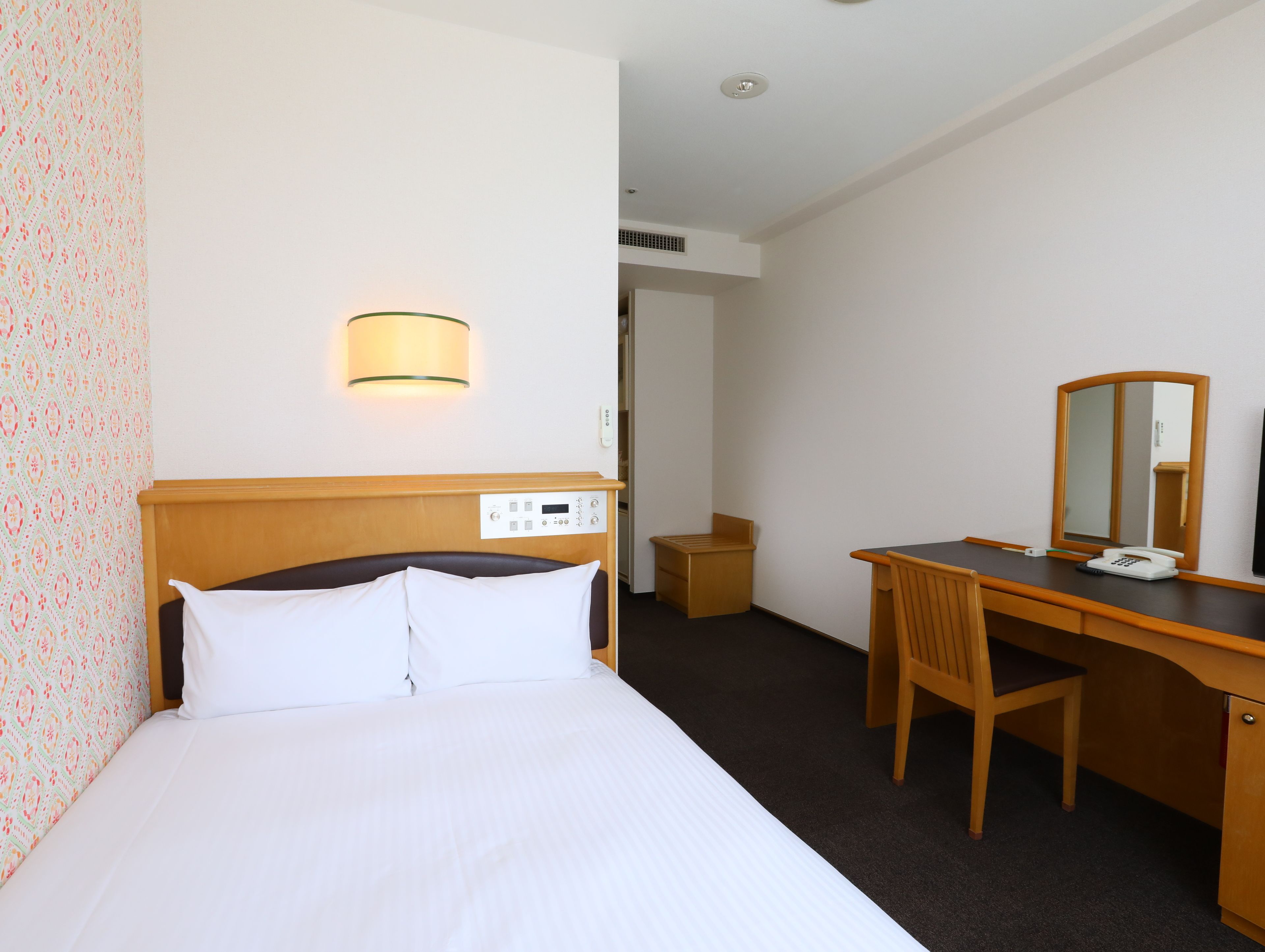 A hotel room with a bed, bedside table, chair, desk, and a mirror.
