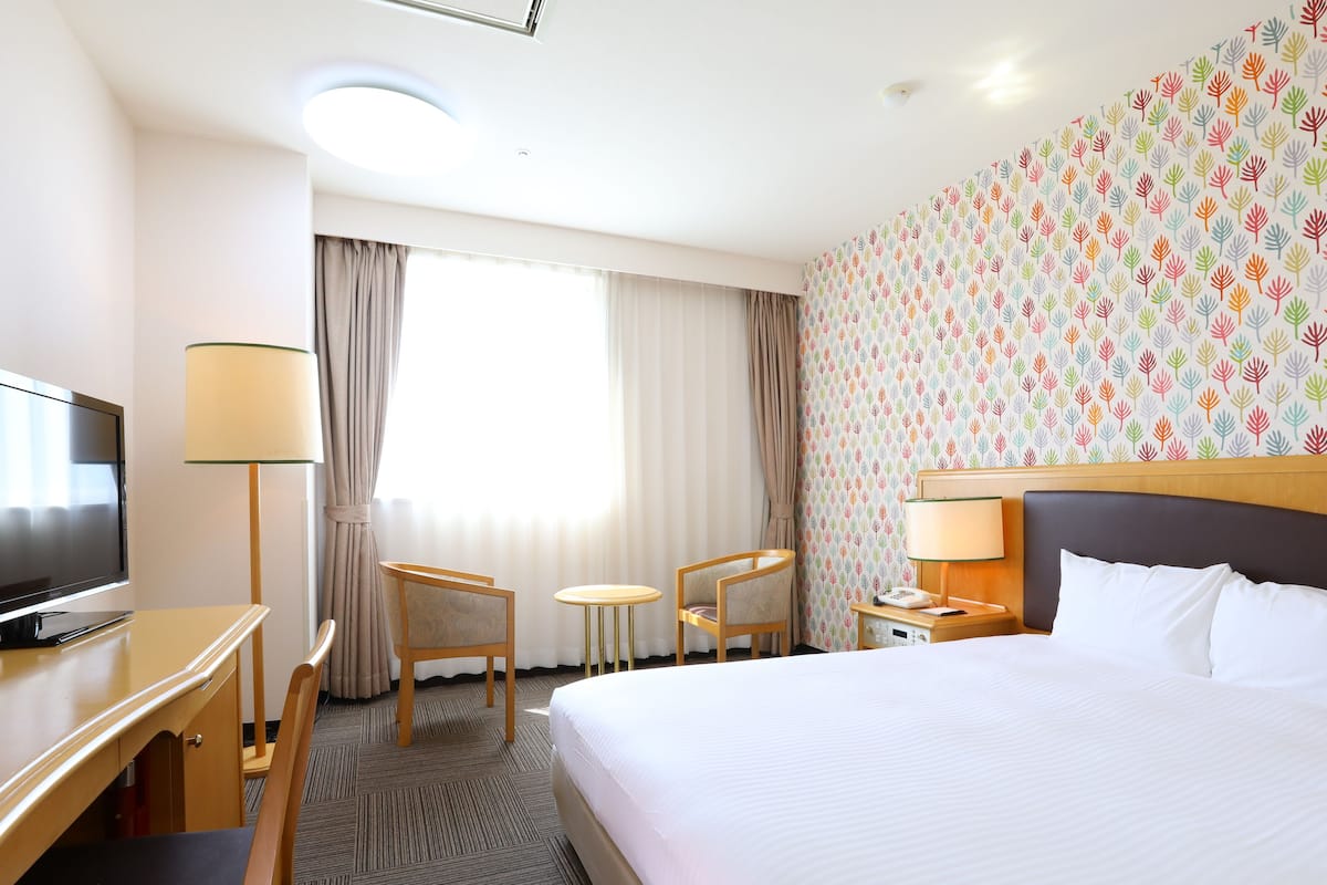 Ein Hotelzimmer mit einem Bett, einem Schreibtisch mit Fernseher, einem Sessel, einem kleinen Tisch und einer Lampe.