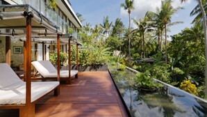 A wooden deck with lounge chairs and a glass-bottomed pool overlooking a tropical garden with palm trees. - Plataran Ubud Hotel & Spa (Ubud)