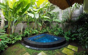 A circular hot tub surrounded by lush tropical plants and a stone wall.
