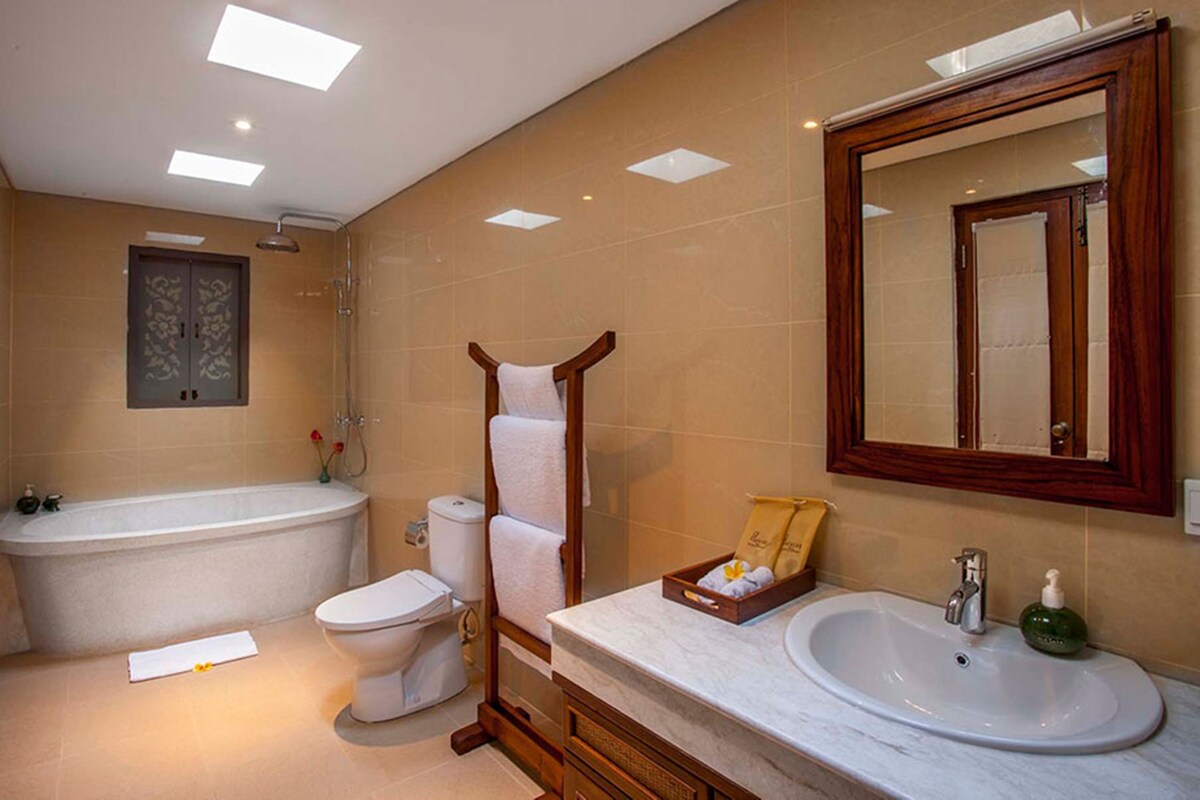 A bathroom with a bathtub, toilet, vanity with a sink, and a large mirror.