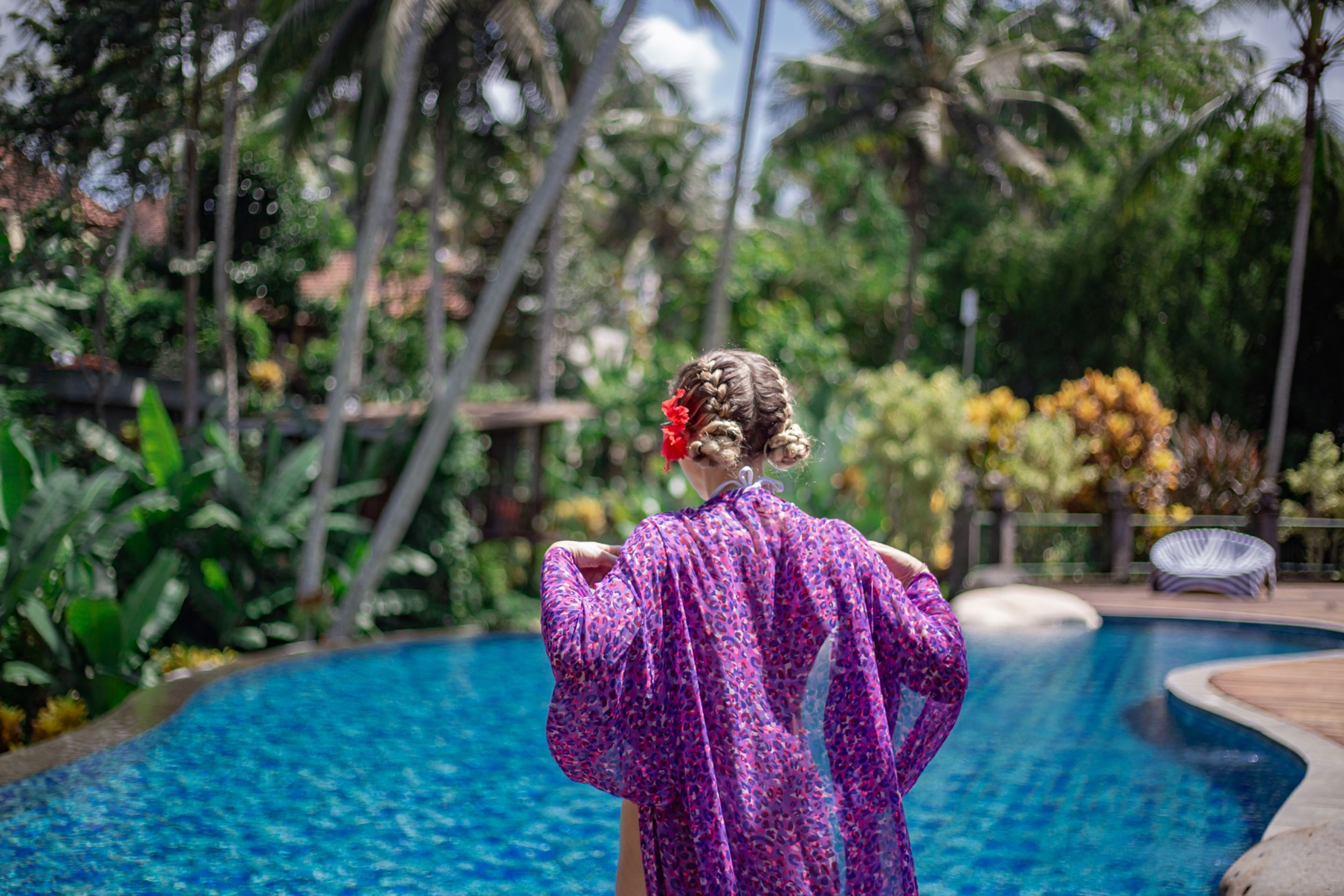 A person standing by a pool with a tropical garden background.