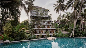 A multi-story hotel with a pool surrounded by tropical vegetation.