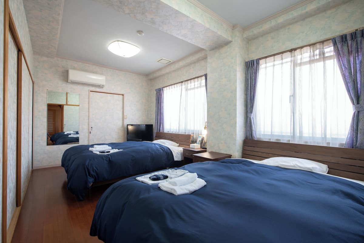 Habitación de hotel con dos camas, un televisor de pantalla plana, aire acondicionado y un ventanal con cortinas.