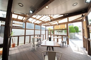 Une terrasse extérieure avec des tables et des chaises en bois, un pot de fleurs et une vue sur la rue.