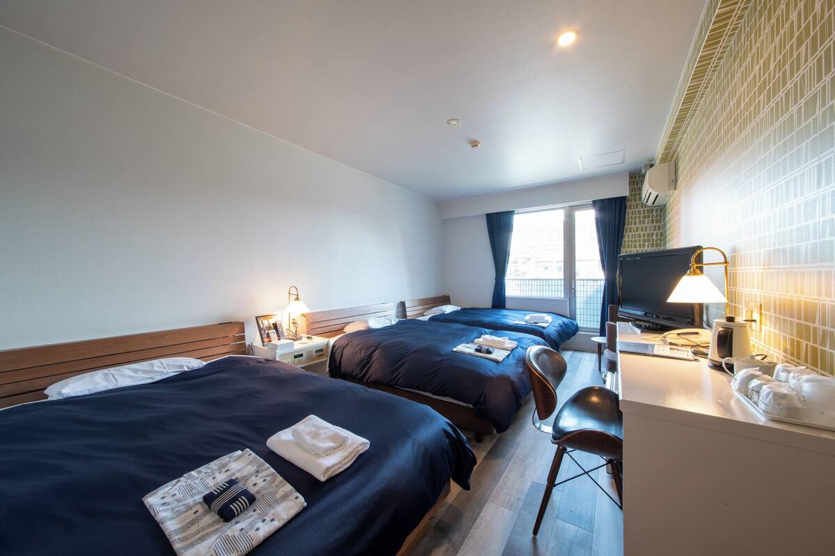 Habitación de hotel con dos camas, un escritorio con computadora, una silla y un televisor.