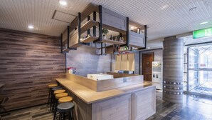 Un área de bar moderna con mostrador de madera, taburetes y una estantería colgante con botellas.